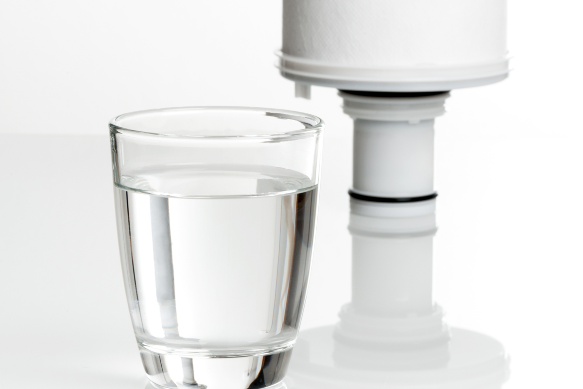 Refil de vela para filtro e copo de vidro com água, em um fundo branco.