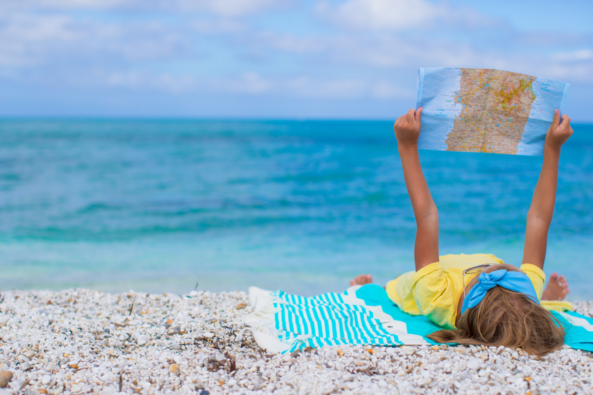 Mulher de amarelo deitada na praia e segurando um mapa.