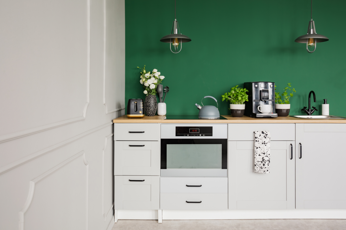 Cozinha simples com móveis brancos e parede verde.
