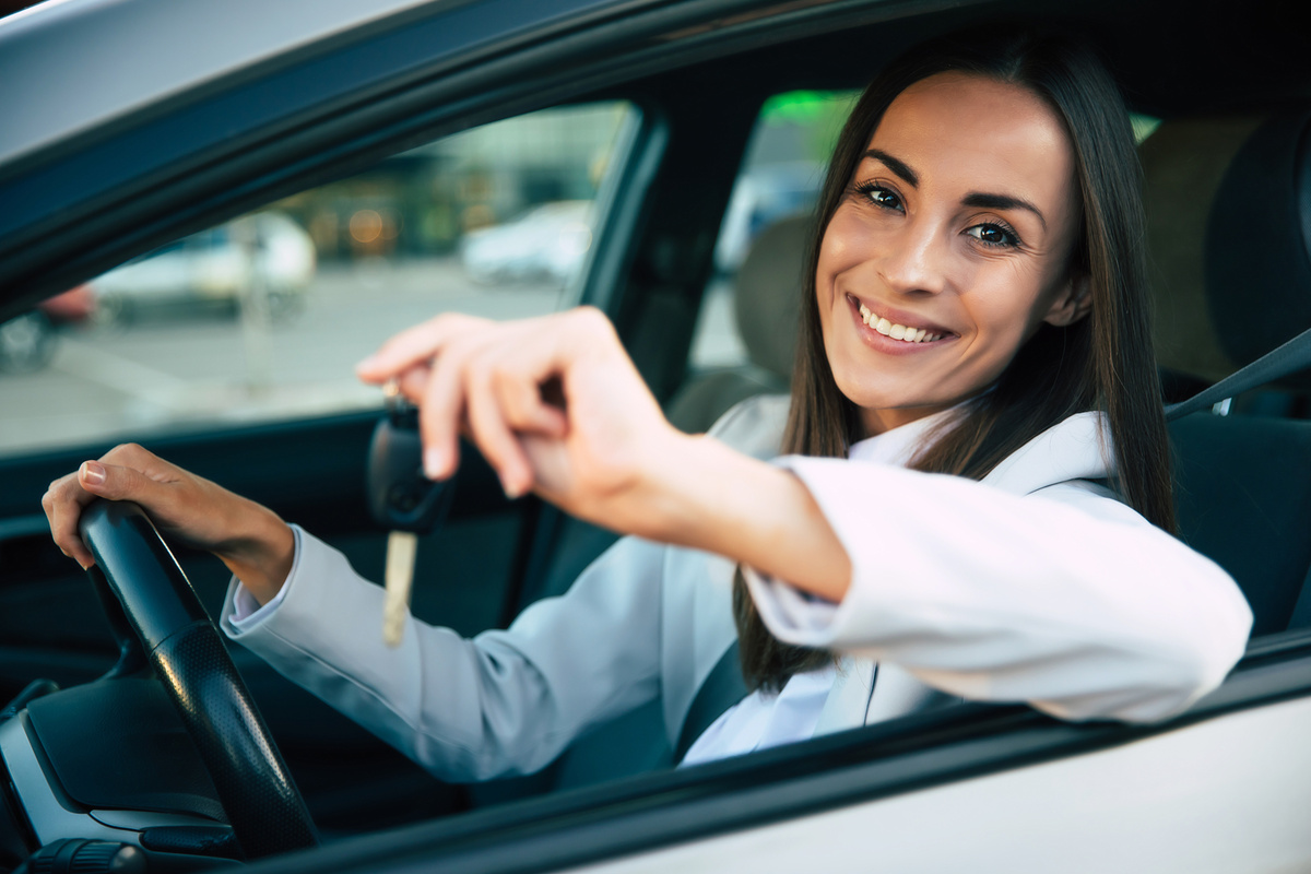 Uma mulher sorrindo dentro de um carro com as chaves nas mãos