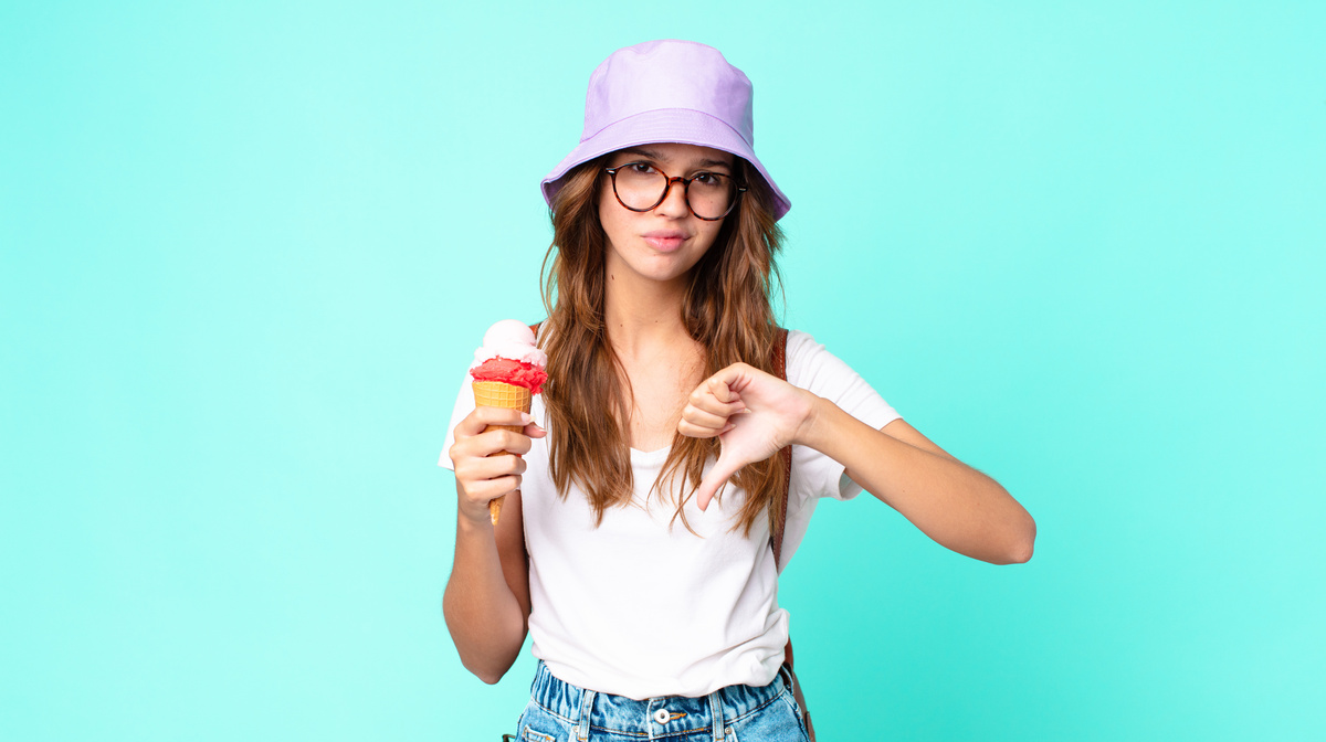 Mulher segurando uma casquinha de sorvete em uma mão e com a outra fazendo sinal de negativo