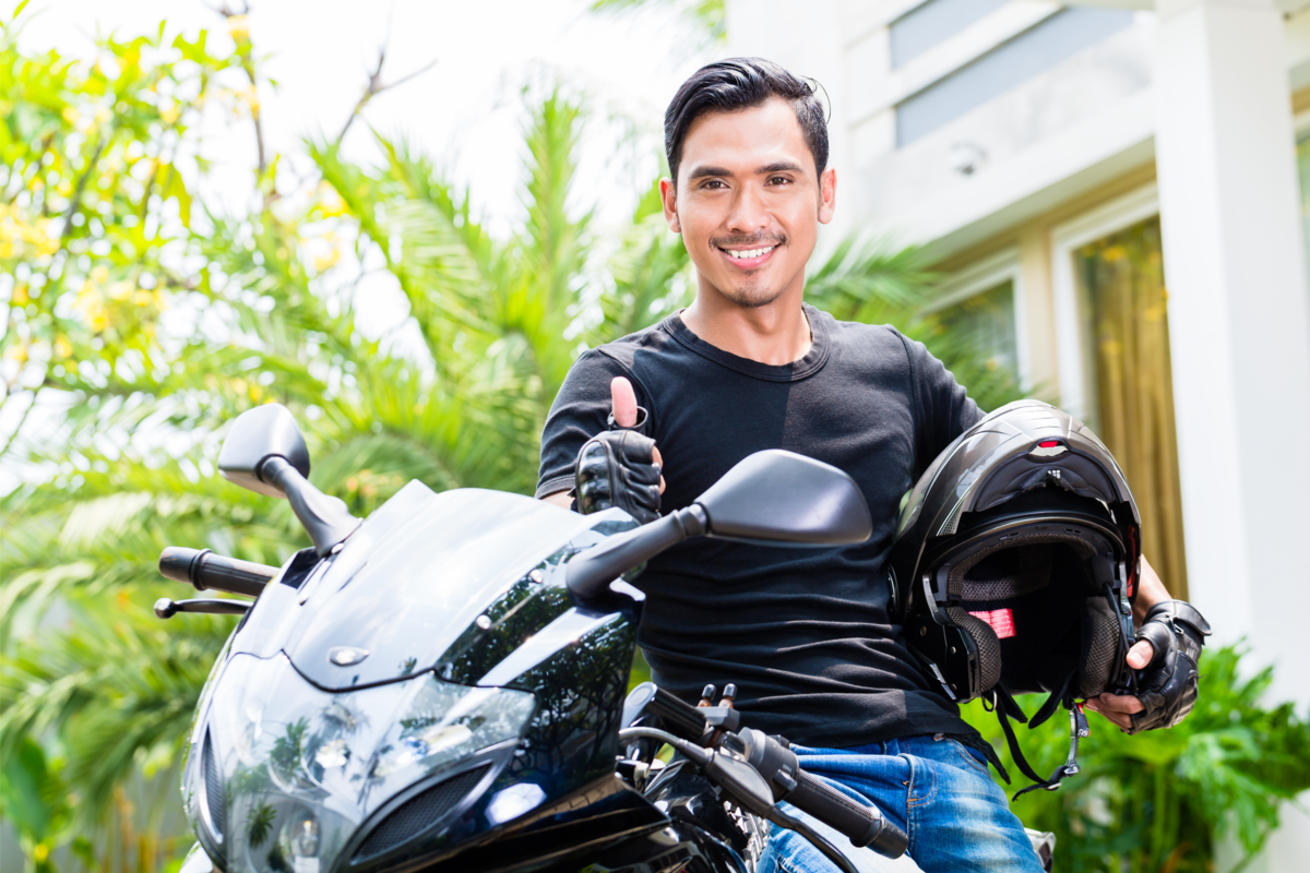 Homem sorridente segurando o capacete e em cima de uma moto Scooter.