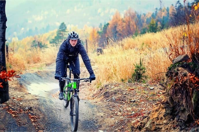 Homem agasalhado fazendo trilha com Mountain Bike no outono