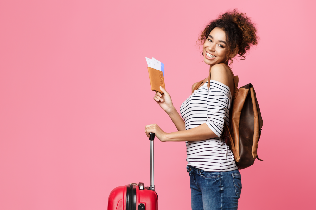Mulher feliz segurando o passaporte e a mala, em um fundo rosa.
