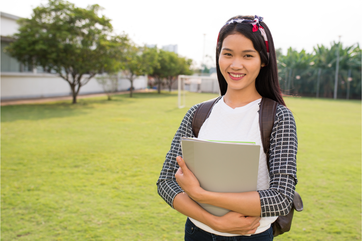 Uma jovem sorrindo segurando o caderno em um campus da faculdade