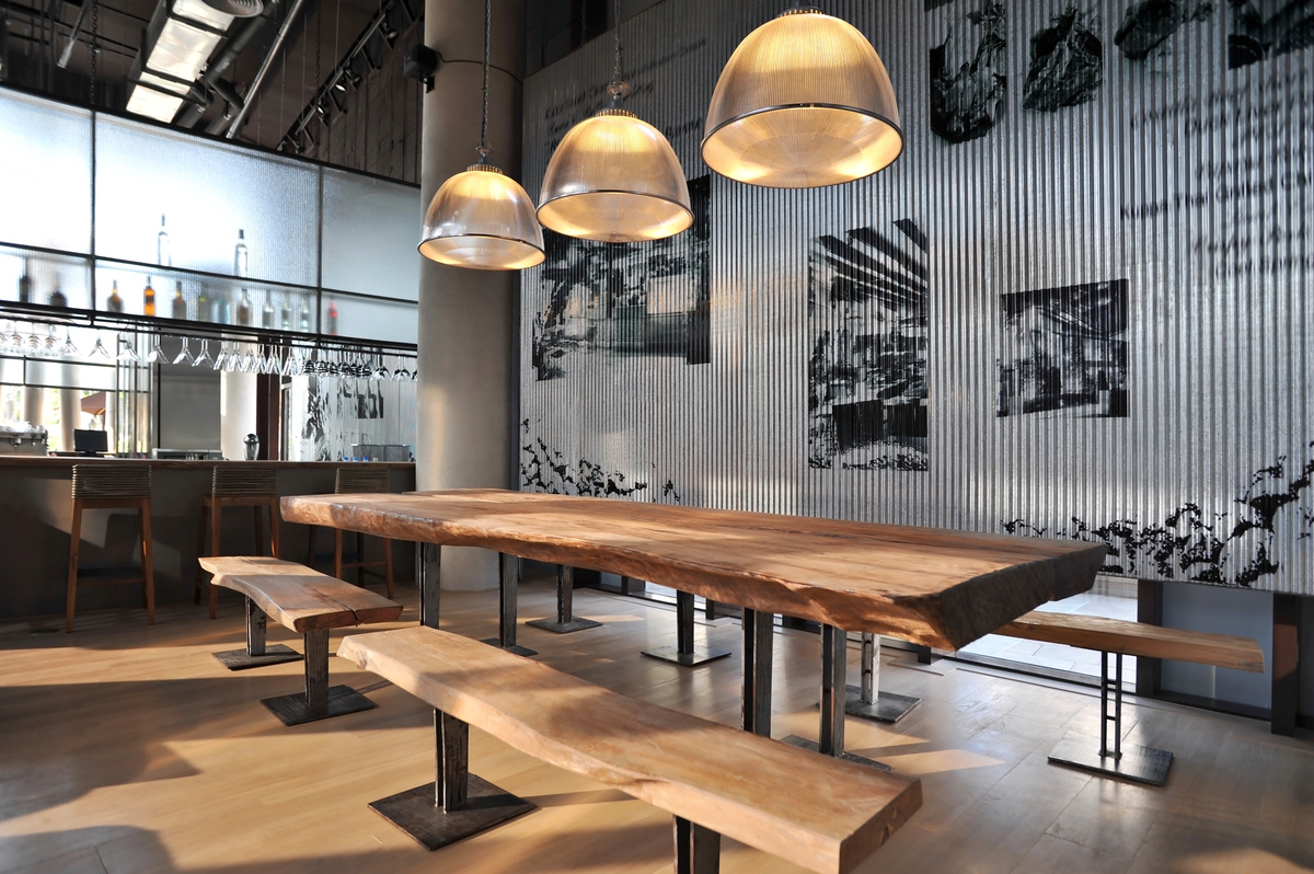 Um bar estilo Industrial com uma bancada para as bebidas e uma mesa e cadeira de madeira