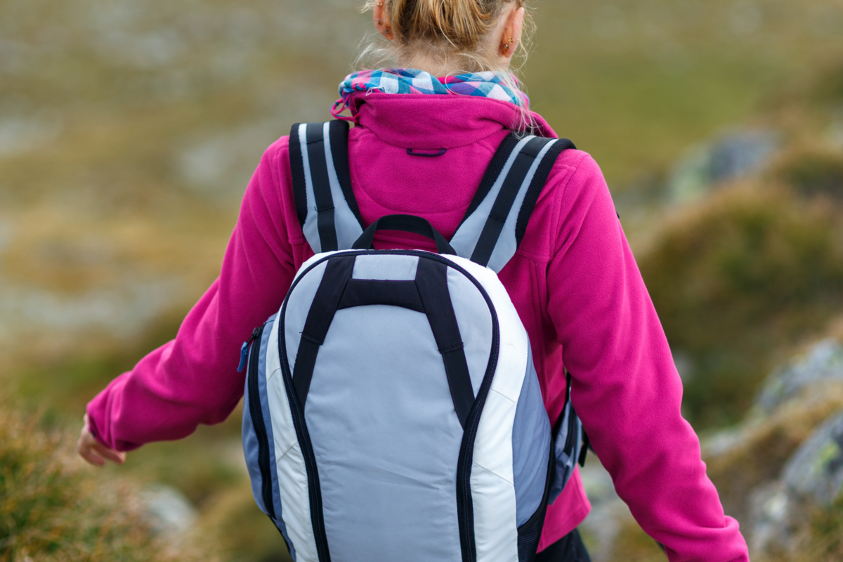 Mulher caminhando em uma trilha e com uma mochila nas costas 