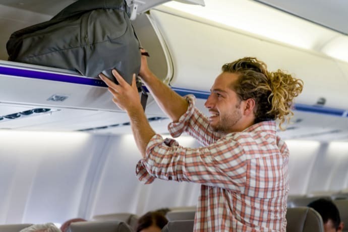 Homem colocando mochila de viagem no compartimento de bagagem interna do avião