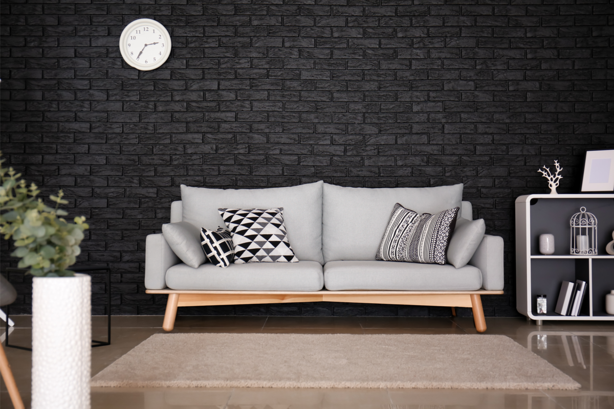 Interior da sala de estar com sofá elegante, perto da parede de tijolos pretos.