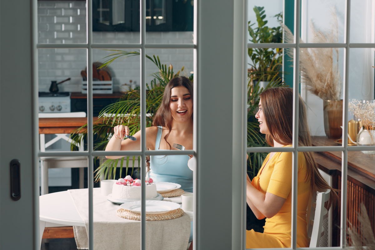 Mulheres em casa sentadas com bolo atrás da porta de vidro.