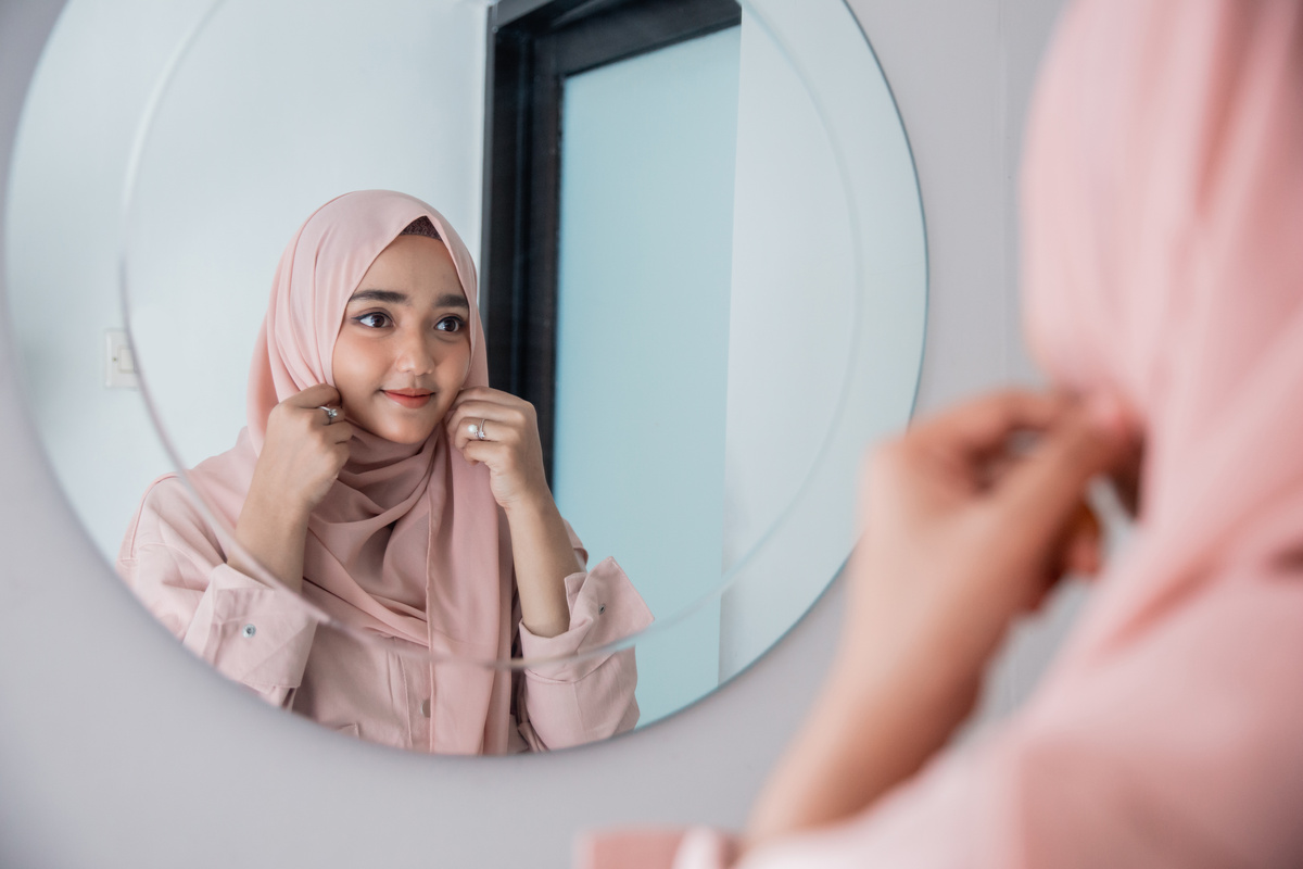 Mulher arrumando hijab sobre cabeça em frente a espelho lapidado