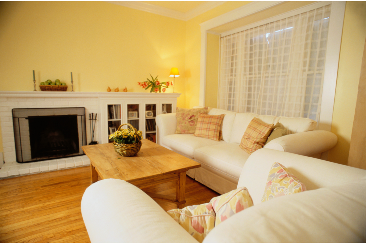 Uma sala com paredes amarelas e sofás brancos e outros móveis de tons claros