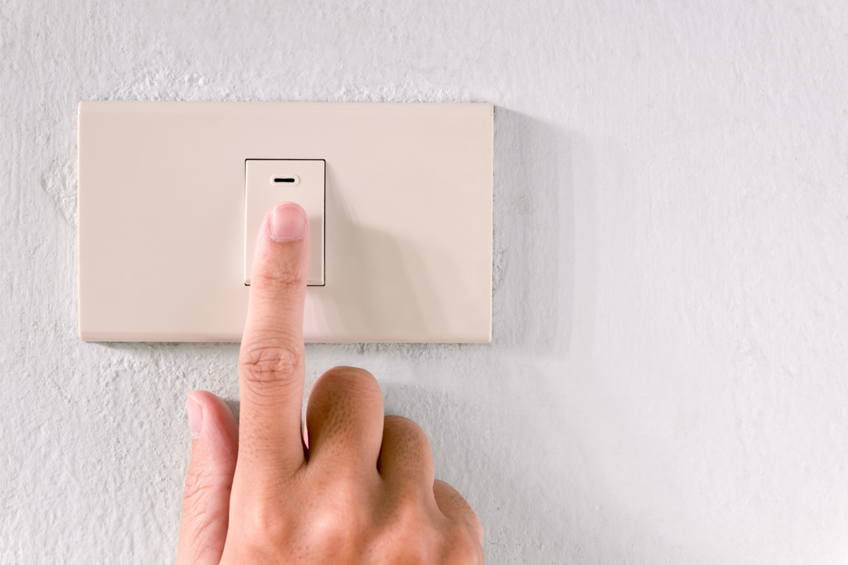 Mão ligando o interruptor bipolar simples em uma parede branca.
