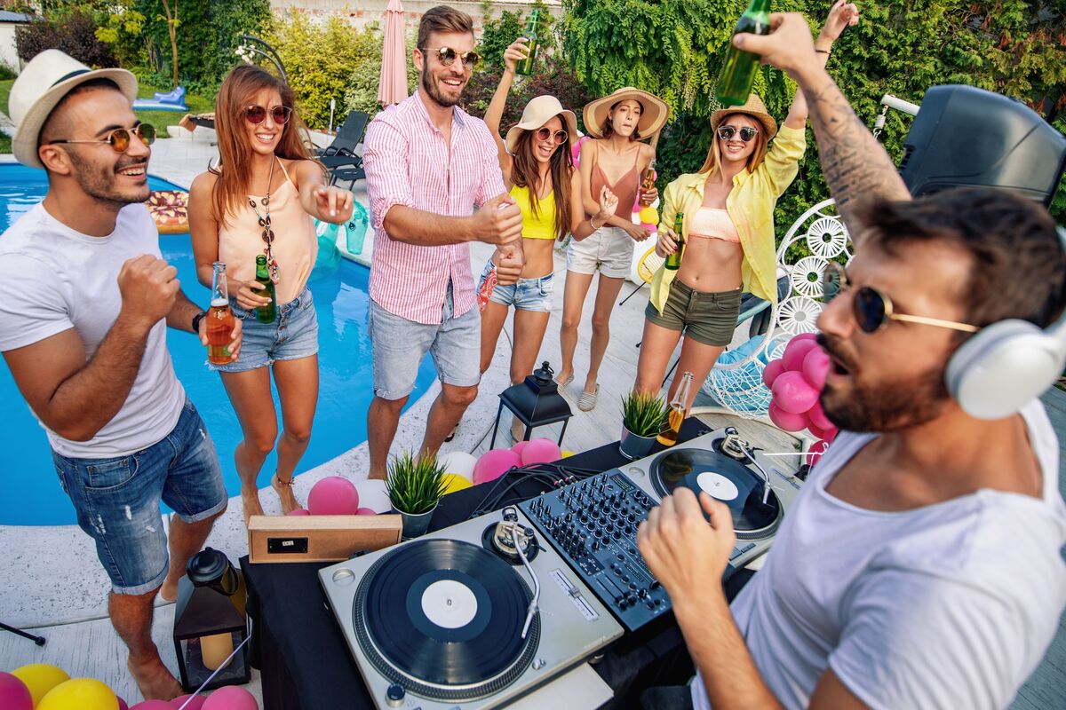 DJ tocando animadamente à beira da piscina e pessoas dançando ao redor