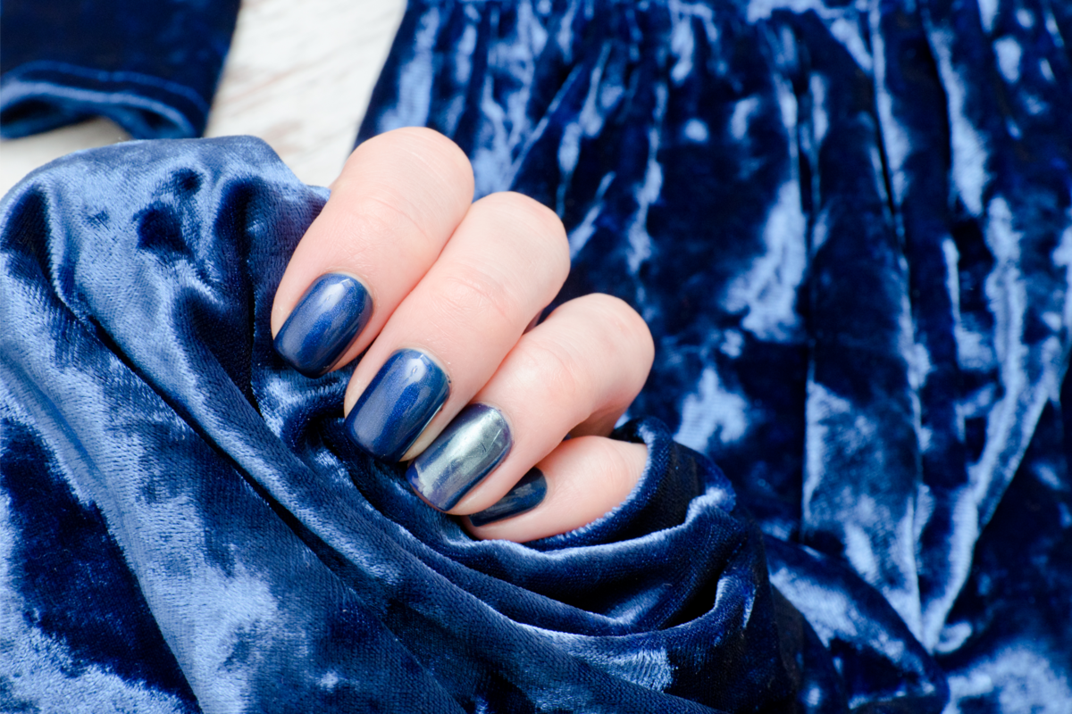 Uma pessoa com unhas azuis segurando um tecido de veludo igualmente azul