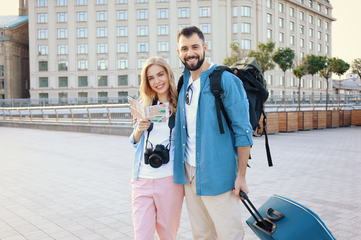 Casal de turistas com câmera, mochila, mala e mapa em uma cidade.