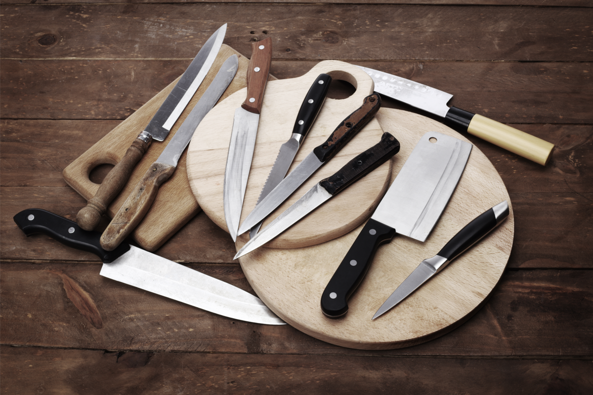 Várias facas de diferentes formatos e materiais, sobre a madeira.