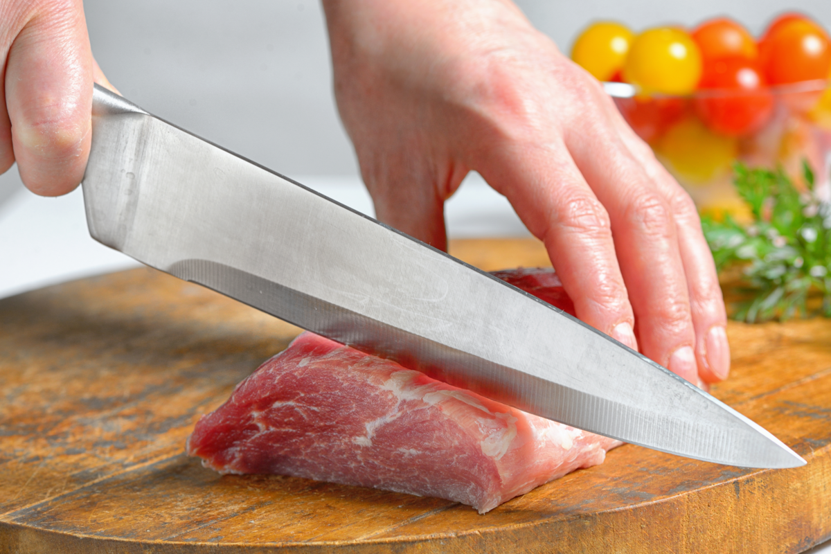 Indivíduo usando uma faca de aço inoxidável para cortar carne.