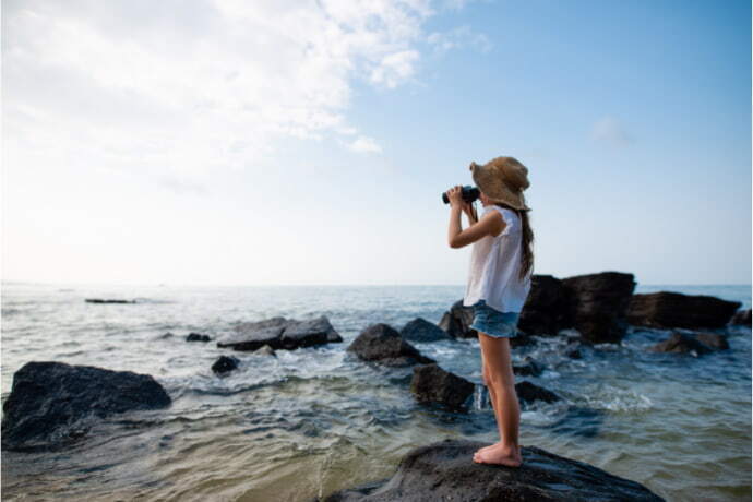 Menina segurando binóculo à frente do mar