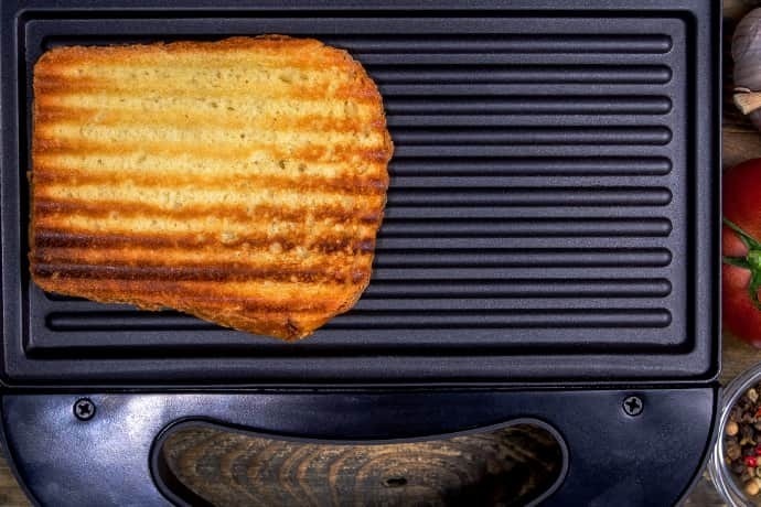Pão sendo tostado em sanduicheira com grill