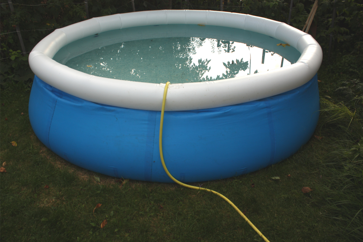 Uma piscina inflável e redonda no jardim com uma mangueira dentro