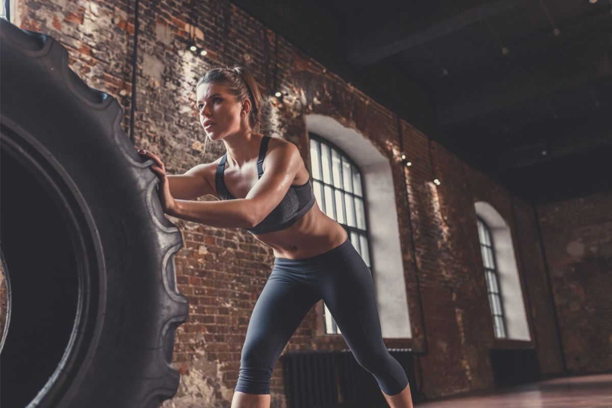 Mulher atlética se exercitando com um pneu grande.