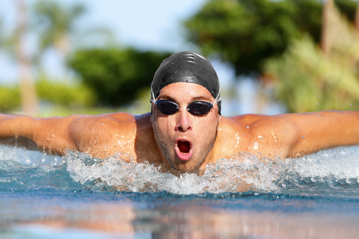Homem com touca e óculos de natação, praticando nado na piscina.