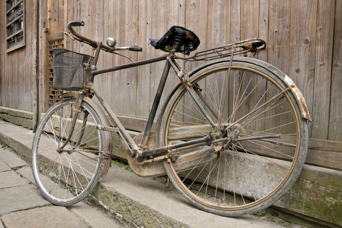Bicicleta antiga e enferrujada próximo da madeira.