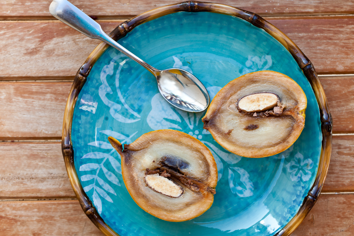 A fruta Abiu em um prato azul com uma colher, sobre a madeira rústica.