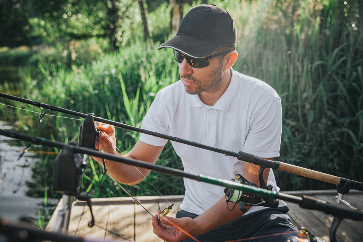 Um pescador em um lago com boné e analisando as varas de pescar