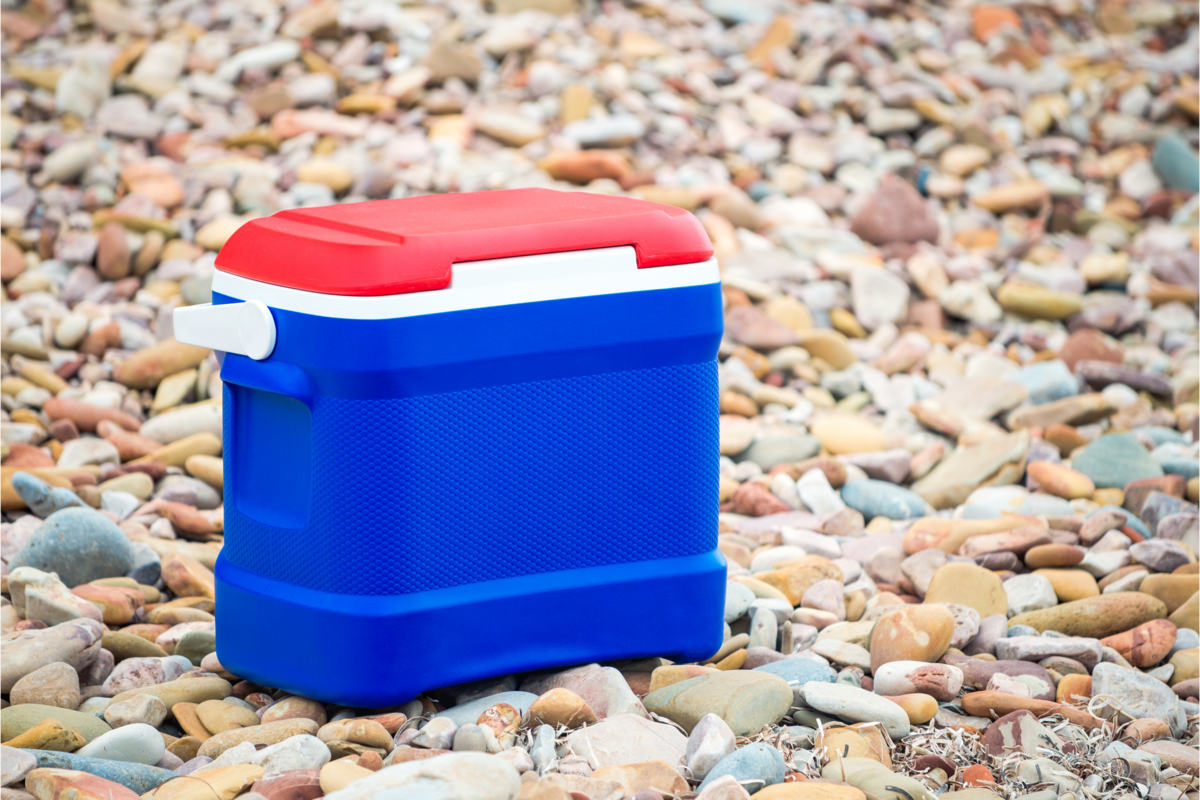 Caixa térmica azul e vermelha em um chão cheio de pedregulhos 