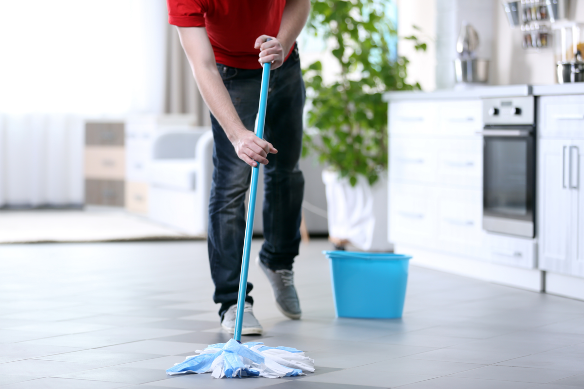 Homem limpando o chão de porcelanato dentro de casa.