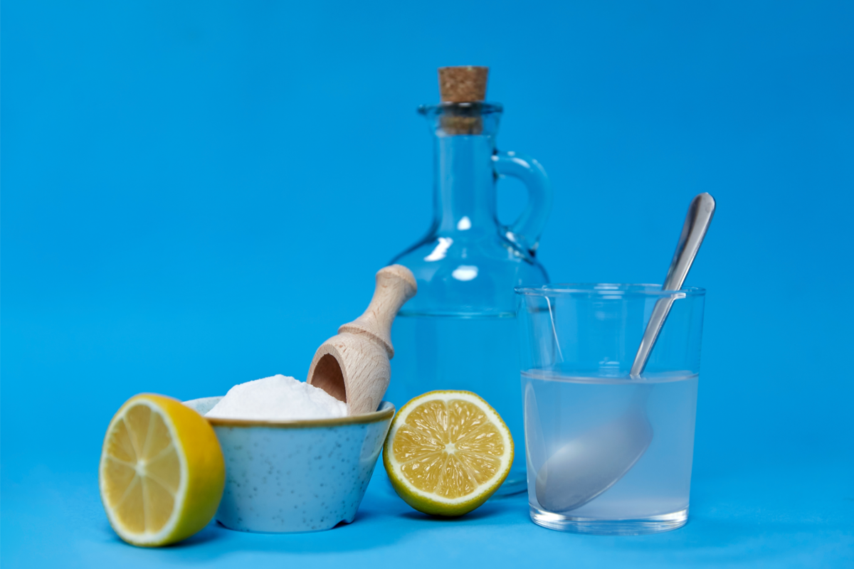 Limões, garrafa de vidro e recipiente com bicarbonato, em um fundo azul.