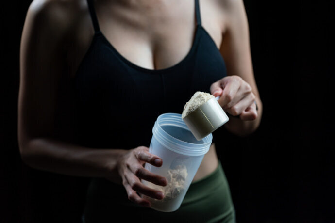 Close-up de mulhere com medida de Whey protein vegano e garrafa de shaker