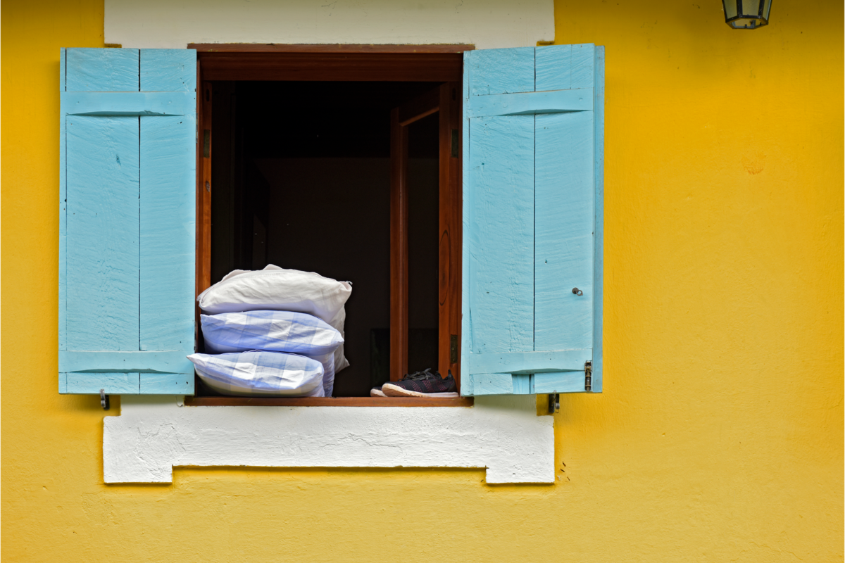 Travesseiros empilhados sobre a janela azul, de uma casa com paredes amarelas.