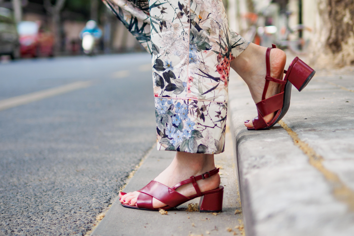 Pés femininos com sandálias vermelhas na calçada de uma rua.