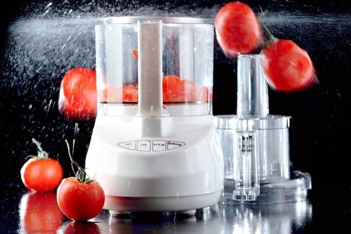 Processador de alimentos com tomates frescos em um fundo preto.