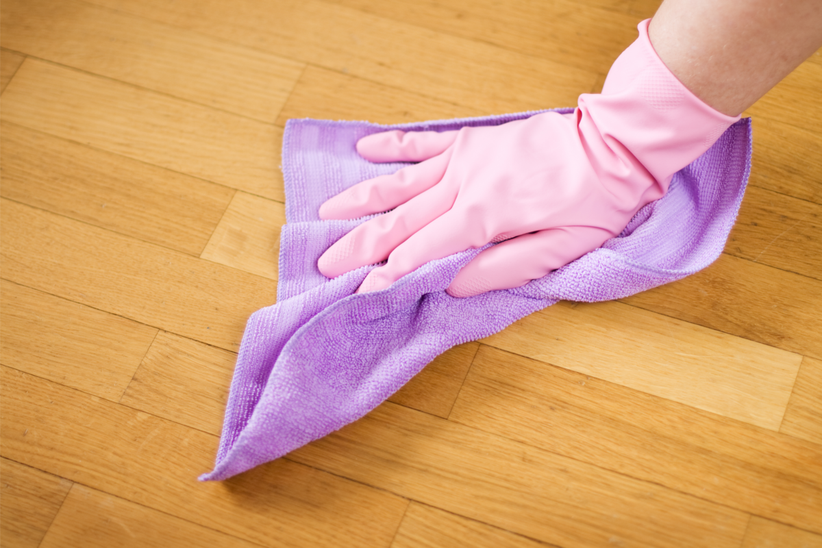 Mãos com luva e um pano limpando o piso