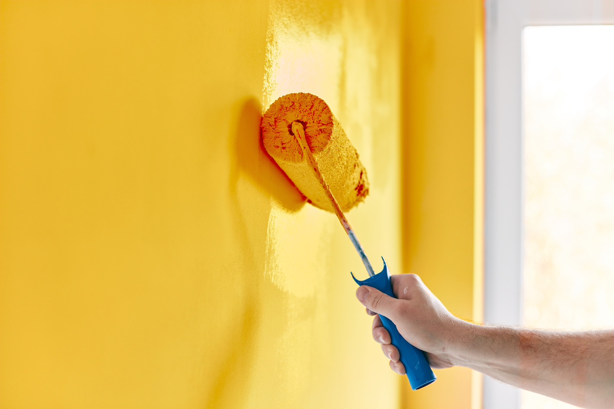 rolo de pintura com tinta amarela contra parede