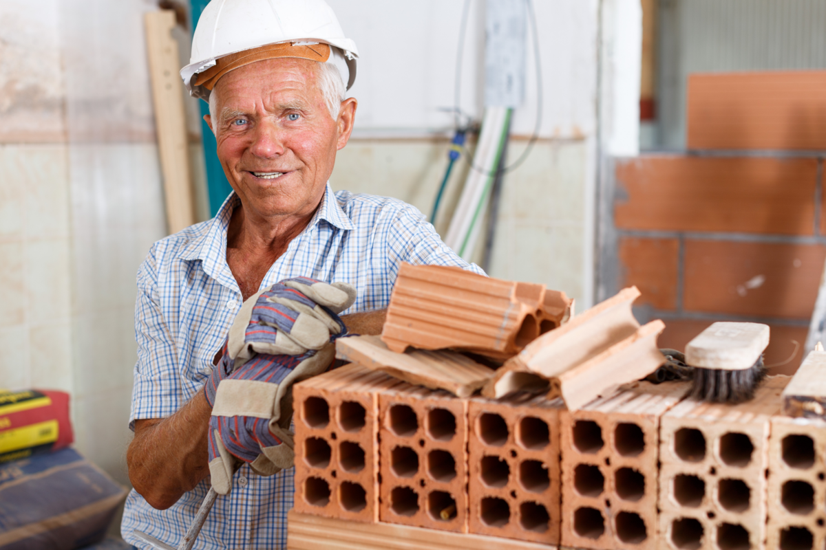 Homem de sorridente próximo de tijolos baianos em uma área de construção.