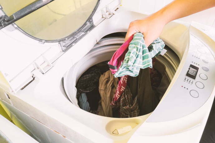 Indivíduo colocando umas peças de roupas no tanquinho de lavar roupa.