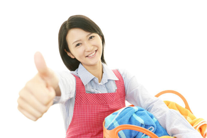 Mulher segurando um cesto de roupas limpas e fazendo um sinal com o polegar de positivo