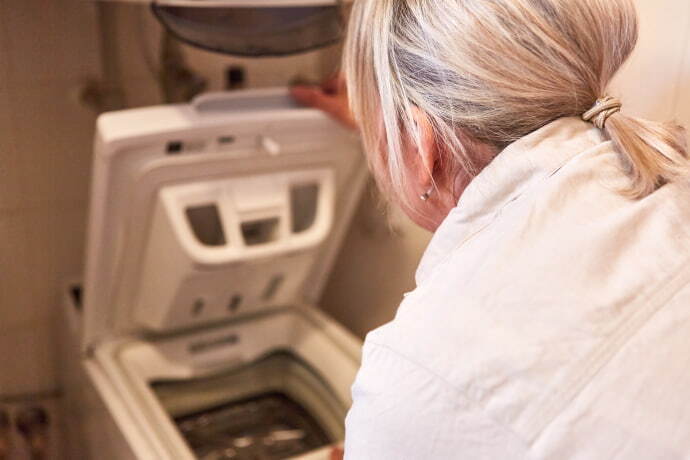 Mulher abrindo a tampa do tanquinho de lavar roupa.