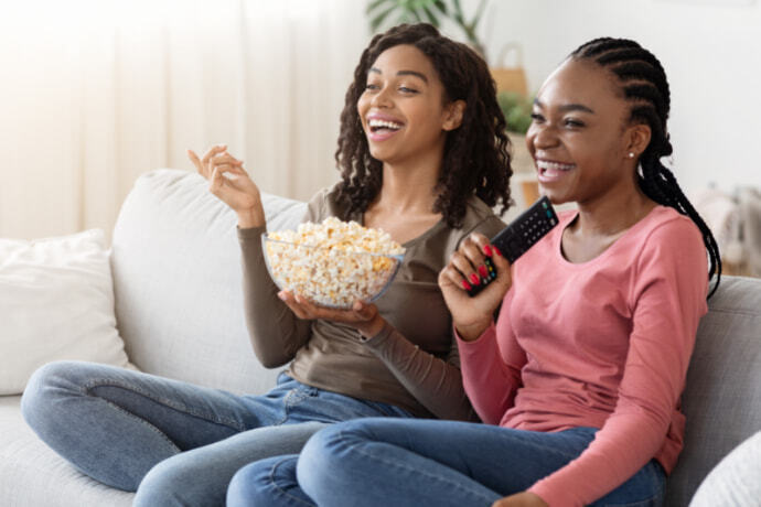 Mulheres assistindo filme no sofá e comendo pipoca 