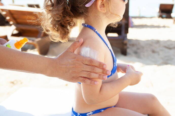 Pessoa aplicando protetor solar na criança
