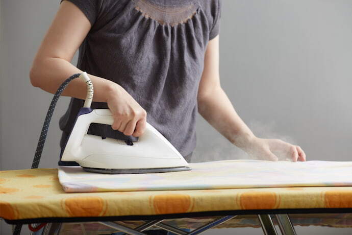 Mulher segurando um ferro branco em uma tábua de passar com vapor.
