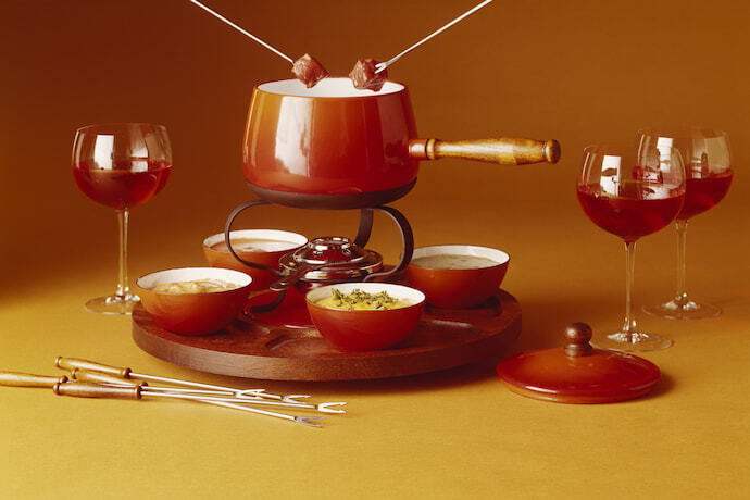 Equipamentos de fondue em uma base giratória sobre mesa e com ingredientes ao redor.