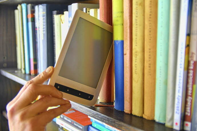 Um e-reader sendo guardado em uma prateleira cheia de livros físicos