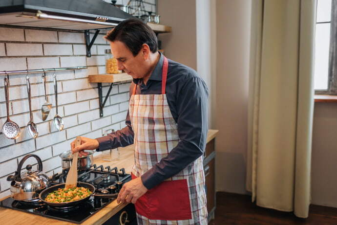 Homem de avental cozinhando no fogão moderno