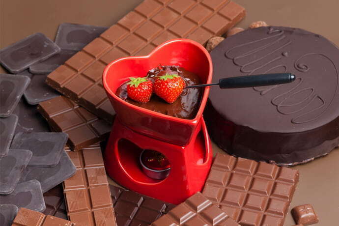 Close-up de um fondue vermelho em formato de coração e cheio de chocolate.